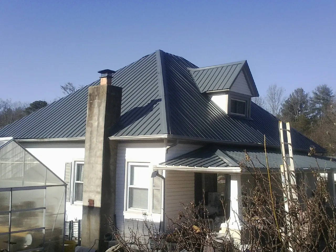 Dark blue standing seam metal roof on a white farmhouse with dormer — Slate & Tile Roof Repair by Roofing Brothers in Dubuque