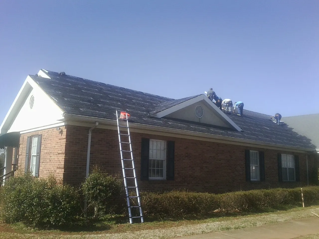 Crew tearing shingles off a brick ranch roof with a ladder set — Metal Roof Repair work by our crew in Dubuque