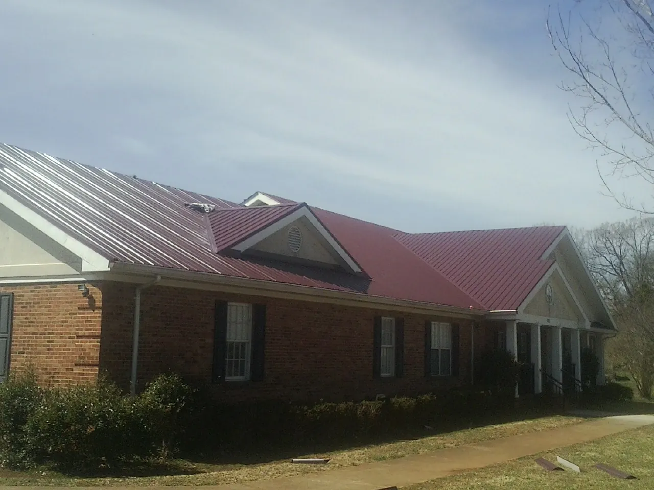 Red metal roof with gabled entries on a long brick building, from a Hail Damage Roof Repair job in Dubuque