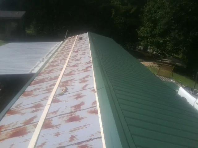 Old rusted panels beside newly installed green metal roofing — Wind Damage Roof Repair by Roofing Brothers in Dubuque