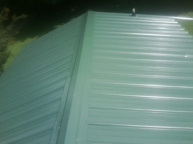 New green metal panels meeting at the ridge of a roof — Flat Roof Repair work by our crew in Dubuque