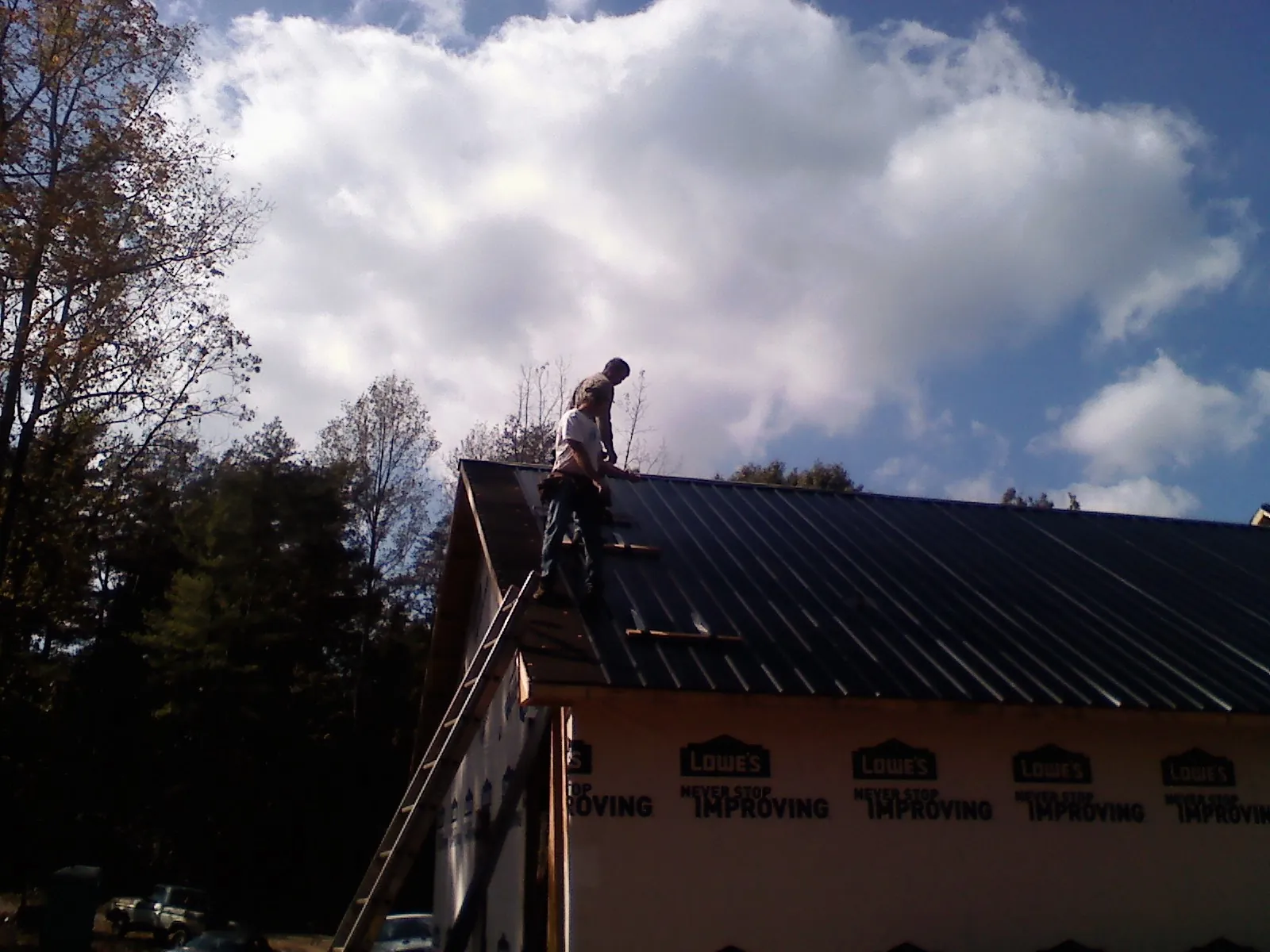 Roofer fastening dark metal panels high against a cloudy sky, from a Roof Inspection job in Dubuque