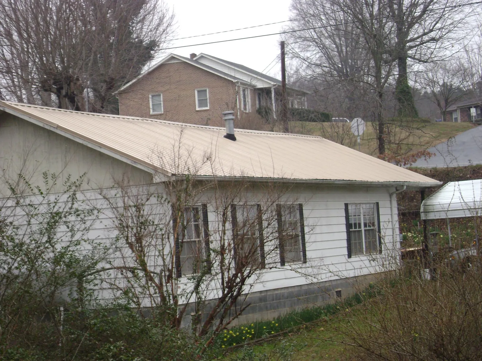 Tan metal roof on a white sided house set into a hillside — Commercial Roofing by Roofing Brothers in Dubuque